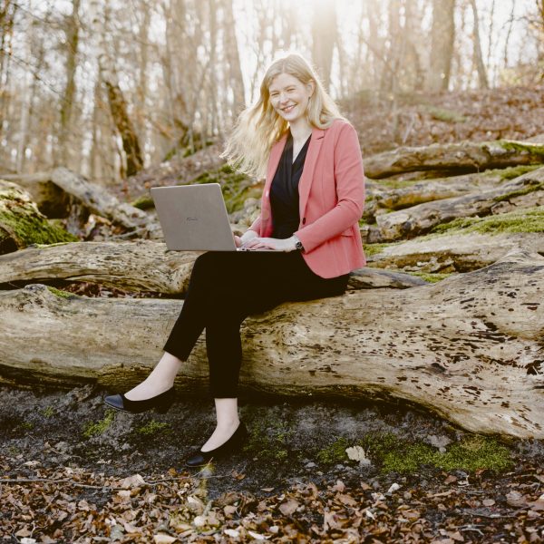 Elisabeth Fechner sitzend auf einem Baumstamm mit Laptop am Schoß