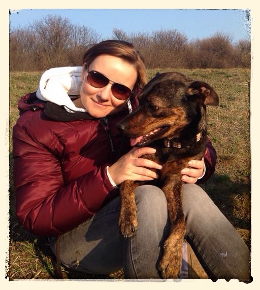 Romy Krenn mit Sonnenbrille am Boden sitzend mit einem Hund Lena über ihre Beine liegend